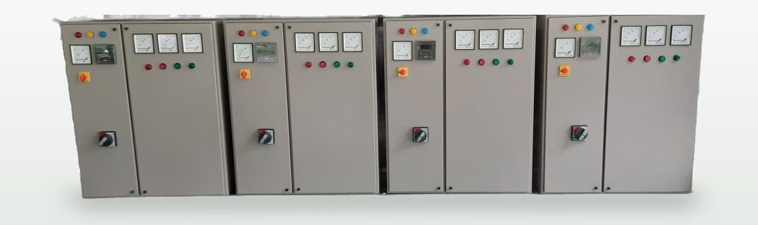 Four completed control panels standing side by side, each with phase indicator lamps, analogue ammeters and voltmeters, start/stop pushbuttons and a rotary isolator